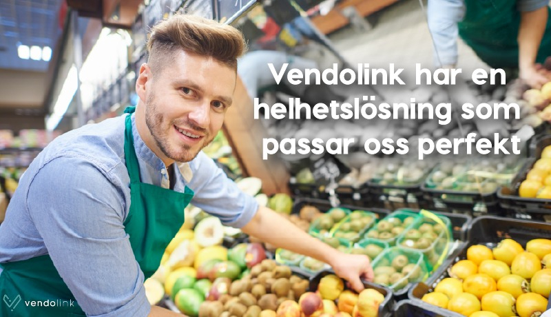En kille med förkläde som står vid fruktavdelningen i en mataffär.