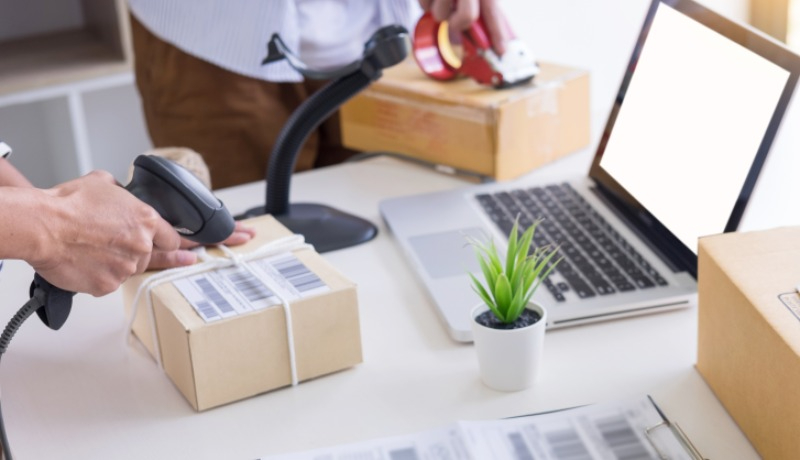En man som skannar ett paket på ett skrivbord framför en laptop.