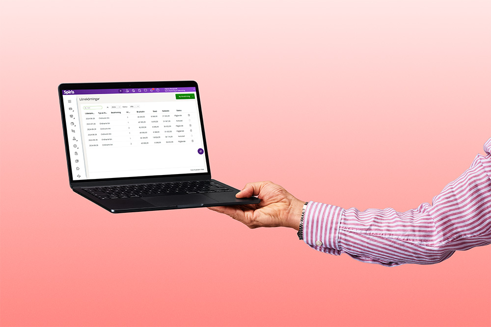 Hand som håller upp en laptop som visar lönekörning på skärmen.