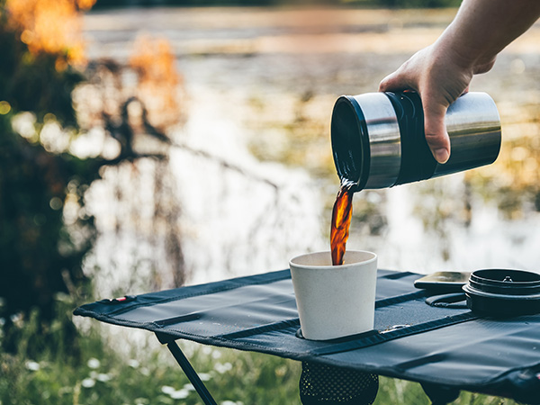 En hand häller kaffe från termos utomhus.