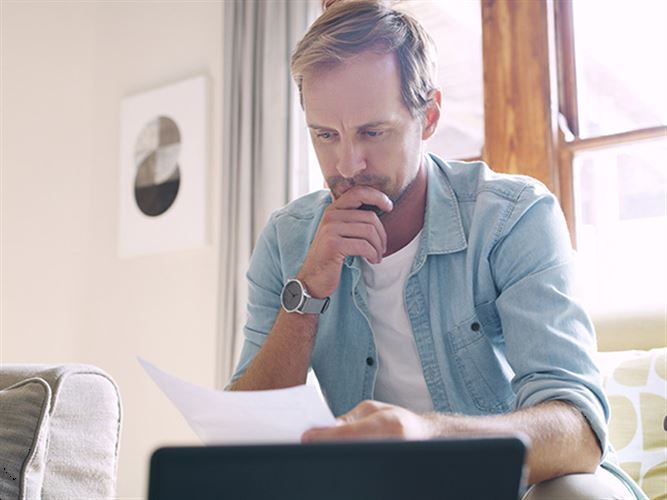 En man som läser ett papper med en dator bredvid sig, som funderar på att välja företagsformer.