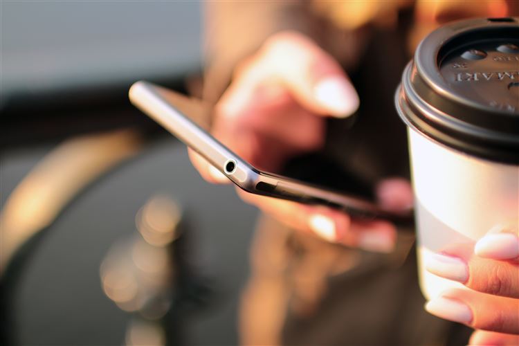 En kvinna håller en kaffe i en hand och en mobiltelefon i den andra där hon arbetar med automatisk bokföring.