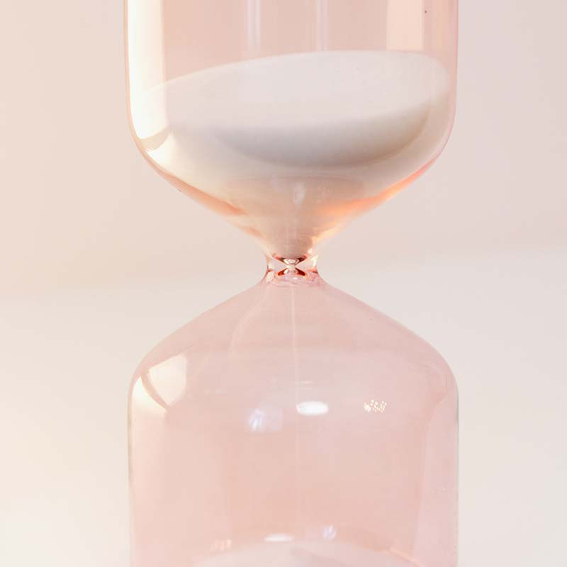 Ett rosa timglas där sanden rinner ner.