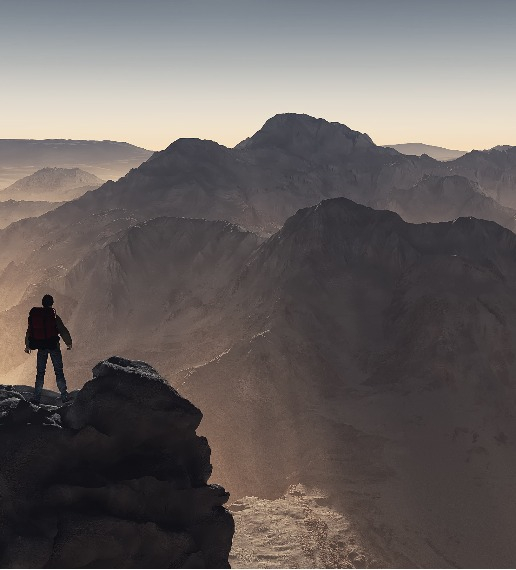 En person står på en bergstopp och tittar ut över en bergskedja.